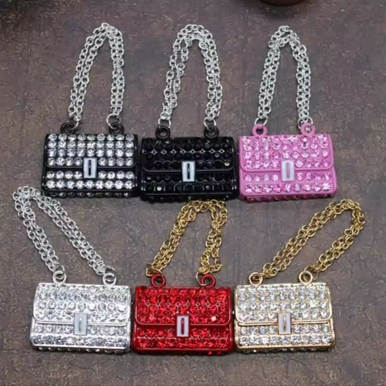 mini handbag-shaped accessories with chain straps, arranged in two rows on a textured brown surface. The top row includes black and pink versions with silver rhinestone-like detailing; the bottom row includes silver, red, and gold versions with similar sparkling embellishments.